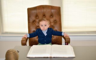 Ein kleiner Junge sitzt auf einem großem Lederstuhl, vor ihm ein Tisch und ein aufgeschlagenes Buch.